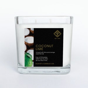 May include: A square glass candle jar with a white candle inside. The label is black with gold text and a gold logo. The label reads "Coconut Lime" and "Infused with lime and orange essential oils". The label also says "Free of Phthalates", "100% Pure Soy Wax", and "40 Hour Burn Time". The label is decorated with a lime and coconuts.