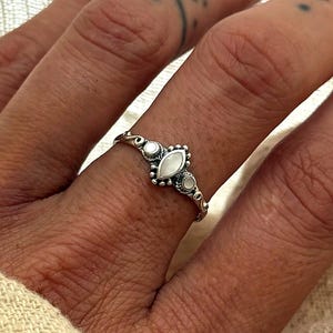 May include: A silver ring featuring an oval, pear-shaped, and round white stone design. The ring is worn on a finger, highlighting the detailed metalwork and the sparkling stones. The ring is a delicate piece of jewellery.