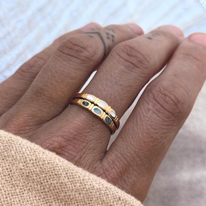 Peut inclure: Deux bagues dorées superposées ornées d'une série de petites incrustations ovales. La bague supérieure présente des incrustations blanches, tandis que la bague inférieure comporte des incrustations ovales vert foncé sur l'anneau métallique.