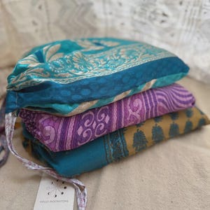 K&ouml;nnte beinhalten: Ein Stapel von drei farbenfrohen Stoffartikeln. Der oberste Artikel ist t&uuml;rkis mit einem floralen Design, der mittlere ist lila mit einem Streifenmuster und der untere ist senfgelb mit einem floralen Muster. Ein Etikett ist angebracht.