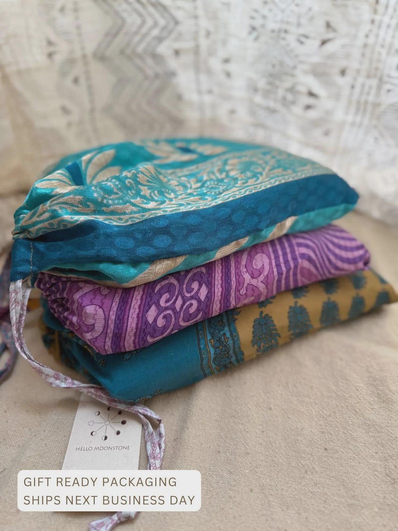 K&ouml;nnte beinhalten: Ein Stapel von drei farbenfrohen Stoffartikeln. Der oberste Artikel ist t&uuml;rkis mit einem floralen Design, der mittlere ist lila mit einem Streifenmuster und der untere ist senfgelb mit einem floralen Muster. Ein Etikett ist angebracht.