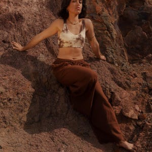 K&ouml;nnte beinhalten: Ein braunes und cremefarbenes Crop-Top mit Batikmuster und eine passende braune Jogginghose. Das l&auml;ssige Outfit wird im Freien getragen und suggeriert Komfort und einen entspannten Stil. Die Kleidung ist f&uuml;r den Alltag geeignet.