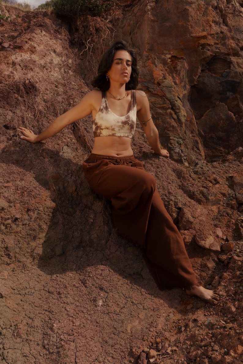 K&ouml;nnte beinhalten: Ein braunes und cremefarbenes Crop-Top mit Batikmuster und eine passende braune Jogginghose. Das l&auml;ssige Outfit wird im Freien getragen und suggeriert Komfort und einen entspannten Stil. Die Kleidung ist f&uuml;r den Alltag geeignet.