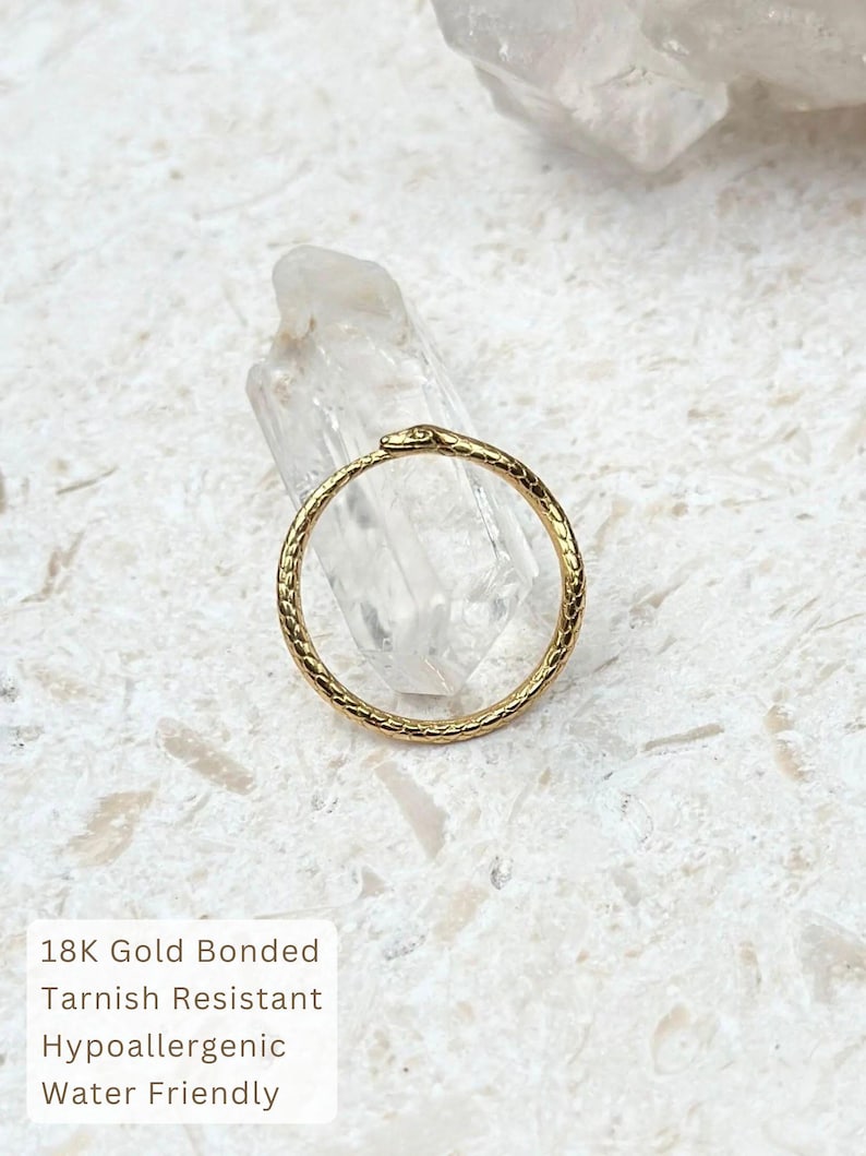 May include: A gold-colored ring with a snake design. The ring is circular with a textured pattern and a snake head at the top. The ring is on a white surface. Text on the image reads: 18K Gold Bonded, Tarnish Resistant, Hypoallergenic, Water Friendly.