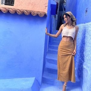 Model wears ankle length skirt with a neatly frayed hemline. The skirt is fitted around the waist and hips with darts and a frayed hem along the waist. The skirt is a caramel colour.