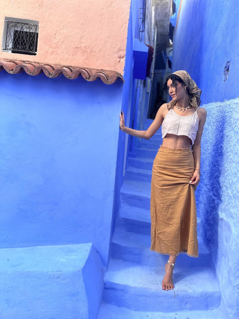 Model wears ankle length skirt with a neatly frayed hemline. The skirt is fitted around the waist and hips with darts and a frayed hem along the waist. The skirt is a caramel colour.