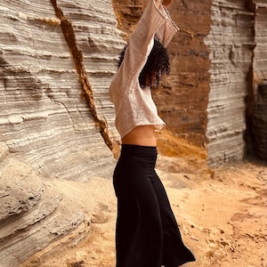 Model wears black stretchy high waisted flare pants. Fitted around the waist and drape well to above the ankle. Soft flowing cotton lycra flared fabric. Model wears pants with cropped long sleeve woven top.