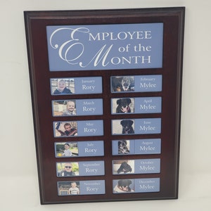 May include: A wooden plaque with a blue background and white text that reads "Employee of the Month". The plaque has 12 photo slots, each with a photo of a person or a dog. The months of the year are listed below each photo slot, along with the name of the person or dog.