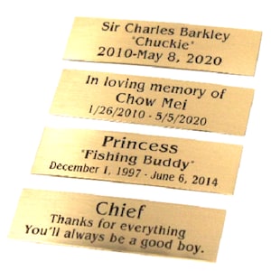 May include: Four gold-colored metal plaques with engraved text. The top plaque reads "Sir Charles Barkley "Chuckie" 2010-May 8, 2020". The second plaque reads "In loving memory of Chow Mei 1/26/2010 - 5/5/2020". The third plaque reads "Princess "Fishing Buddy" December 1, 1997 - June 6, 2014". The bottom plaque reads "Chief Thanks for everything You'll always be a good boy."