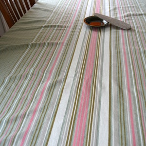 Puede incluir: Un mantel de mesa a rayas en tonos de blanco, gris, verde y rosa. Un pequeño plato marrón y un utensilio de madera se colocan sobre el mantel.