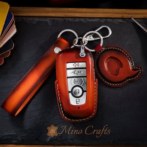 Peut inclure: Un porte-clés en cuir marron avec une clé de voiture argentée à l'intérieur. Le porte-clés a une boucle pour l'attacher à un porte-clés. La clé a des boutons pour verrouiller, déverrouiller et d'autres fonctions. Le porte-clés est marqué "Mino Crafts".