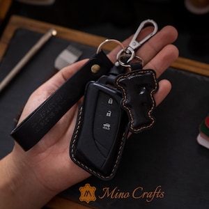 May include: Black leather key chain with a black leather key fob and a black leather letter F charm. The key fob has a silver car key with three buttons, one labeled "HOLD".
