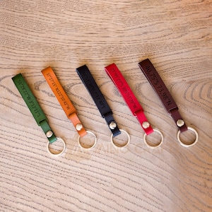 May include: Five leather keychains with metal key rings. Each keychain has a different color and features coordinates engraved on the leather strap. The coordinates are: 40,75°S 73,98°N, 21°01′27″S 105°51′28″W, 48'51'30 B 2"17'40"E, 37°27′15" N122°10′43″W, and 51°28′22″W 3°12′11″S.