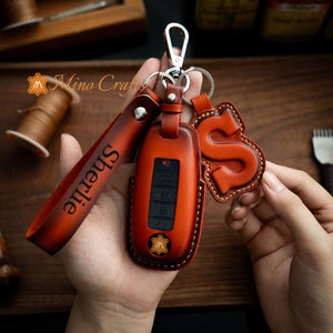 May include: A brown leather key chain with a key fob and a leather charm with the letter "S" on it. The key fob has a black button and the text "Sherrie" is embossed on the leather strap.