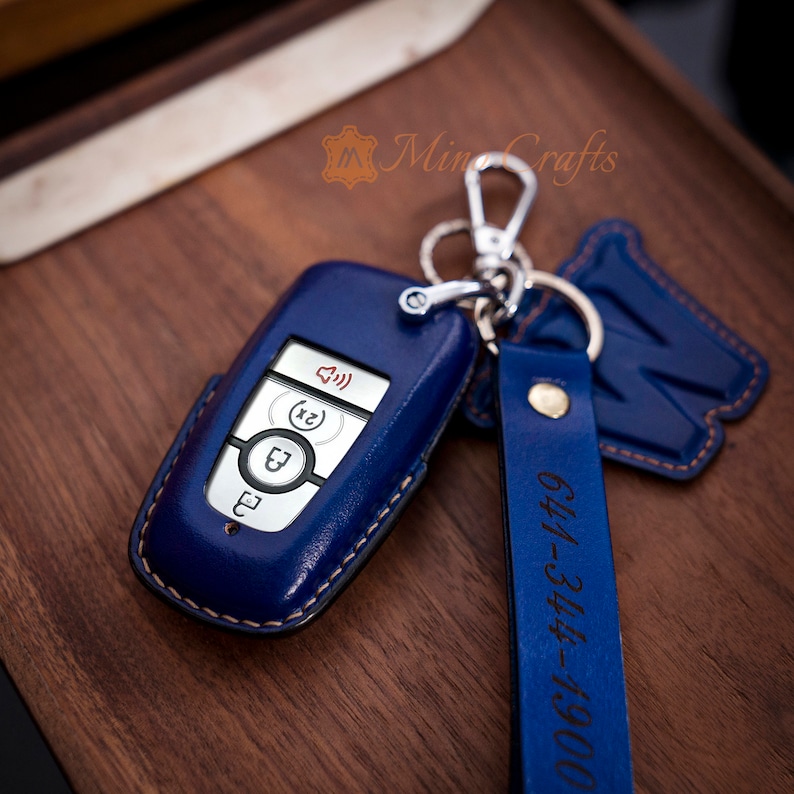 May include: A blue leather key fob with a silver key chain and a blue leather strap with the text "0001-344-4149" in black. The key fob has a silver car key with buttons.