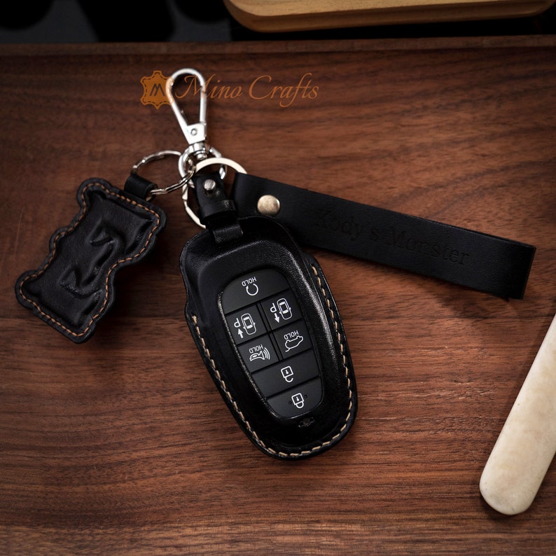 May include: Black leather key fob with a stitched edge and a silver key ring. The fob has a black leather strap with the text "Royce Register" embossed on it.