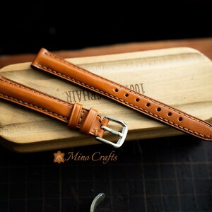 May include: Two brown leather watch straps with stitching. One strap has a silver buckle.