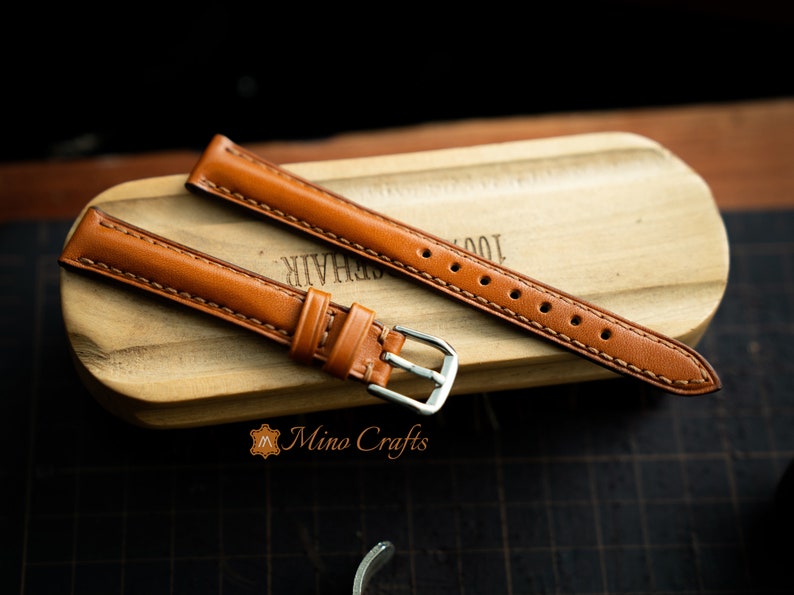 May include: Two brown leather watch straps with stitching. One strap has a silver buckle.
