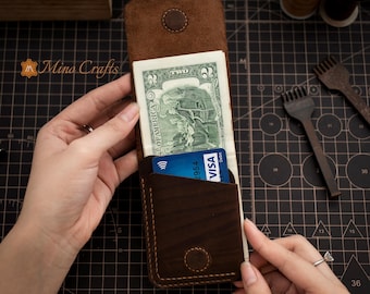 May include: A brown leather wallet with a flap that opens to reveal a two dollar bill and a credit card. The wallet has a stitched edge and a small circle design on the front.