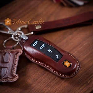 May include: A brown leather key fob with stitching around the edges. The fob has four buttons with symbols on them. The fob has a small leather tag with the letter "M" on it.