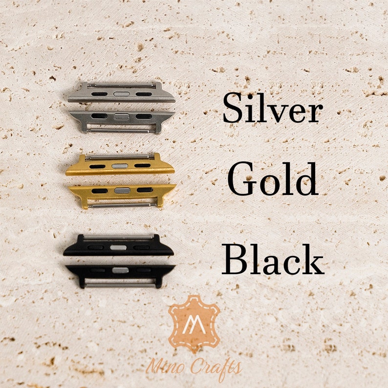 May include: Three Apple Watch band adapters in silver, gold, and black. The adapters are made of metal and have a polished finish.
