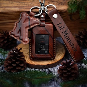 May include: A brown leather key fob with a wood grain pattern and a key chain with a leather strap that says "Lil Monster".