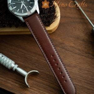 May include: A brown leather watch strap with a stitched edge and multiple holes for adjusting the fit. The strap is attached to a silver watch with a black face and the word "CASIO" printed on it.