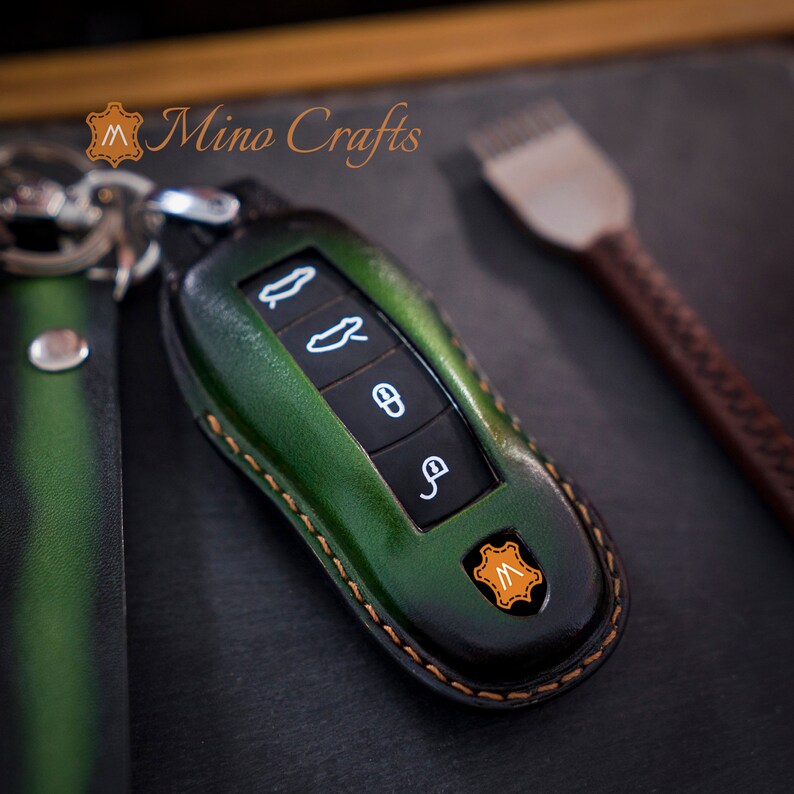 May include: Green leather key fob with stitching around the edges. The fob has four buttons and a small leather tag with the letter "M" on it. Mino Crafts is printed on the background.