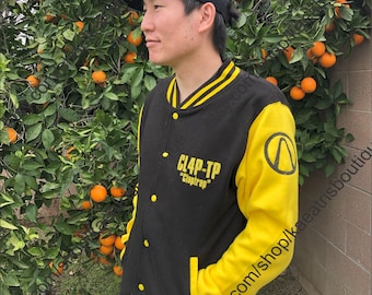 May include: Black and yellow varsity jacket with the text "CL4P-TP" and "Claptrap" on the chest. The jacket has yellow sleeves and a black body with yellow stripes on the collar and cuffs. A black baseball cap is worn.