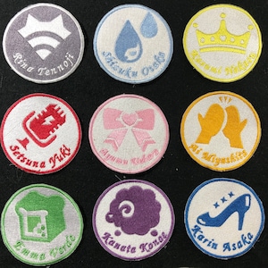 May include: Nine embroidered patches with white backgrounds and colorful designs. The patches feature various symbols and text, including a crown, a microphone, a drop of water, a bow, a pair of gloves, a loaf of bread, a sheep, and a high heel shoe.