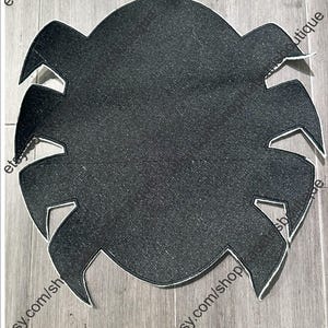 May include: A black, spider-shaped placemat with a white border. The placemat has a textured surface and is designed with eight pointed legs. The Etsy shop URL is visible in the image.