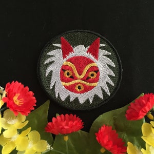 May include: An embroidered patch featuring a stylised animal face in red and white. The patch is set against a dark green background and has a white fluffy border.
