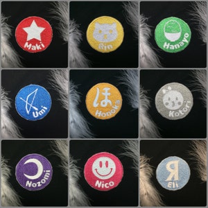 May include: Nine colorful embroidered patches with different designs and names. The patches are circular and feature a star, a cat, a bowl of shaved ice, an arrow, a Japanese character, a panda, a crescent moon, a smiley face, and a letter 'R'.