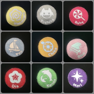 Puede incluir: Nueve parches redondos bordados de colores vivos con diferentes diseños y nombres. Los parches incluyen una flor, un barco, un limón, un piano, una piruleta, un delfín, una estrella, un remolino y un monstruo.