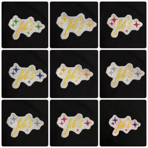 Pode incluir: Nove patches bordados com fundo branco e estrelas douradas, azuis, vermelhas, amarelas, roxas e laranja. Os patches apresentam o texto "Ju's" em uma fonte cursiva.