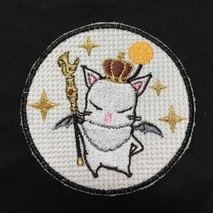 May include: White embroidered patch with a cartoon cat wearing a crown and holding a staff. The cat has wings and is surrounded by stars.
