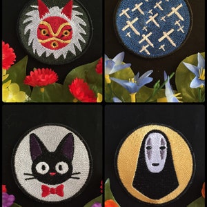 May include: Four embroidered iron-on patches featuring characters from the animated film Spirited Away. The patches are circular and feature No Face, the spirit of the forest, Jiji the black cat, and a symbol of the bathhouse.