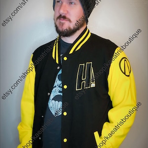 May include: A black and yellow varsity jacket featuring a letter H on the chest, a circular logo on the sleeve, and yellow striped ribbed trim on the collar and cuffs. The jacket has a button-front closure and long yellow sleeves.