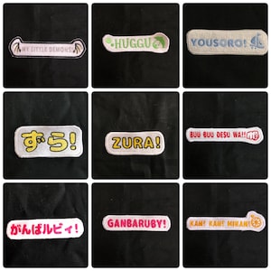 Puede incluir: Nueve parches bordados con varios diseños y textos. Los parches son blancos con texto y diseños coloridos. El texto en los parches incluye "My Little Demons", "Huggu", "Yousoro!", "ずら!" (Zura!), "BUU BUU DESU WA!!", "ZURA!" (Zura!), "がんばルビィ!" (Ganbaru-bi!), "GANBARUBY!" y "KAN! KANE MIKANI".