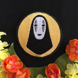 Op de afbeelding: Een ronde geborduurde patch met een wit No Face-personage uit de animatiefilm Spirited Away. Het personage is omgeven door een gele cirkel met een zwarte omtrek.