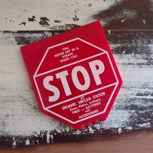 May include: Red octagonal stop sign with white lettering that reads "You never get in a scrape when you STOP at Uhlmans Sinclair Station Cross Plains, Indiana Tires - Batteries and Accessories".