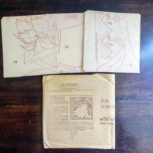May include: Vintage sewing patterns and a packet from "The Workbasket" magazine. The patterns feature floral and geometric designs, with the numbers 94, 96, and 97 visible. The packet includes text and an illustration of an apron. The items are on a dark wooden surface.