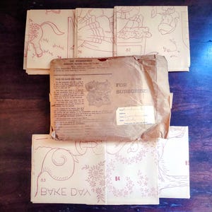 May include: A collection of vintage paper ephemera, including pattern sheets and a brown paper envelope. The pattern sheets feature red line drawings of figures and designs. The envelope has text that reads "FOR SUBSCRIBER".