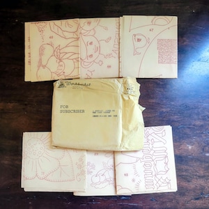 May include: A collection of vintage sewing patterns and a subscription envelope. The patterns feature red line drawings of fruits, flowers, and other designs. The envelope is labeled "For Subscriber" and includes the text "The Workbasket".