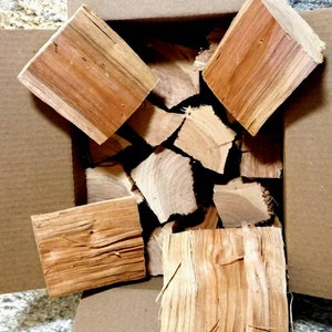 May include: A cardboard box filled with pieces of wood for smoking. The wood is a light brown color and has a natural grain pattern.
