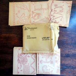 May include: A collection of vintage craft patterns and ephemera. The image shows several small booklets with red illustrations and text, along with a yellow envelope labeled "The Workbasket" and "For Subscriber."