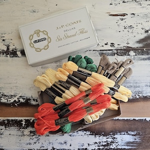 May include: A white cardboard box labeled J. & P. Coats Deluxe Six Strand Floss containing multiple skeins of embroidery thread in shades of orange, yellow, green, and brown. Each skein features a black paper band with the J. & P. Coats brand name.