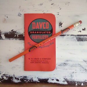 以下が含まれることがあります： 「DAVCO GRANULATED FERTILIZER」と会社名「W. R. GRACE & COMPANY」が表紙に印刷された赤い小冊子。小冊子の隣には、「DAVCO」と印刷されたオレンジ色の鉛筆がある。