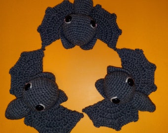 May include: Three gray crocheted bats with black eyes and pink noses are arranged in a circle on a bright orange background.