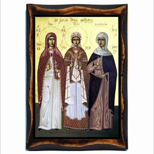 May include: An icon depicting three figures in religious garments, set against a gold backdrop. The image is framed in a dark, rustic wooden frame. Each figure holds a cross and has a halo.